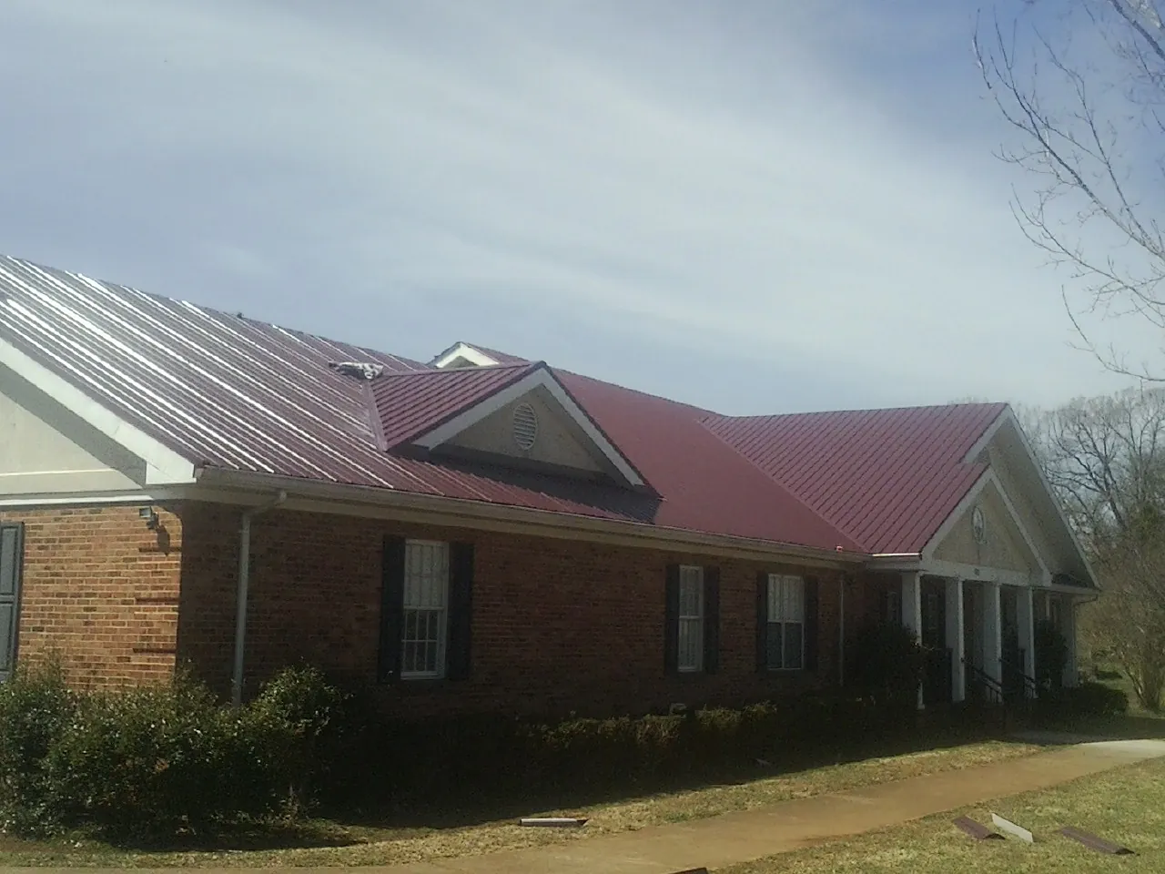 Red metal roof with gabled entries on a long brick building, from a Hail Damage Roof Repair job in Wallula